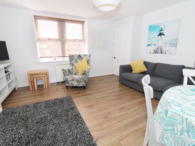 A living room with a gray sofa and patterned armchair with yellow cushions at Sunnie Cottage in Seahouses