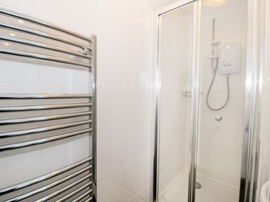 A shower cubicle with glass doors and a chrome heated towel rail in a bathroom at Sunnie Cottage in Seahouses