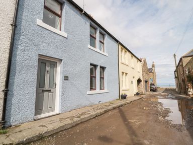 A row of houses along a dirt street with puddles including a blue house with a gray door and a yellow house at Sunnie Cottage in Seahouses