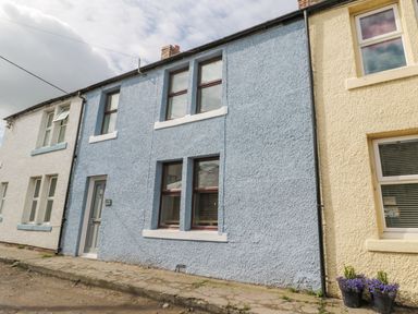 The front exterior of a blue two story house with four windows and a gray door on a paved street at Sunnie Cottage in Seahouses