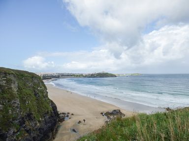 A beach with sand and waves next to cliffs and grassy land at 5 Ocean Heights in Newquay