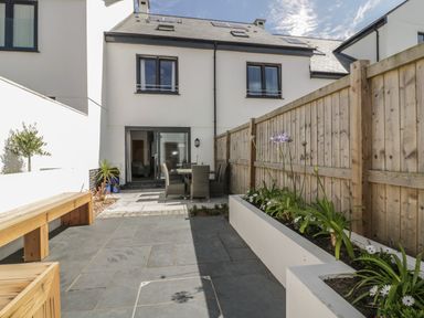 A patio area with a wooden bench and dining table with chairs surrounded by a wooden fence and plants at 5 Ocean Heights in Newquay