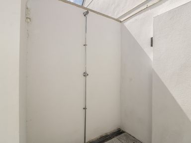 An outdoor shower with a metal showerhead and handle mounted on white walls at 5 Ocean Heights in Newquay