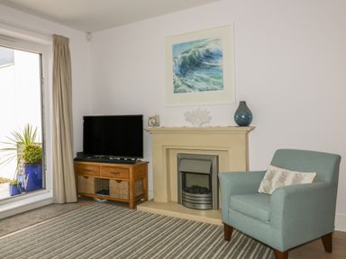A living room with a fireplace TV on a wooden stand an armchair and a painting of a wave at 5 Ocean Heights in Newquay
