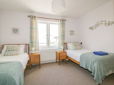 A bedroom with two single beds separated by wooden nightstands and a window with plaid curtains at 5 Ocean Heights in Newquay