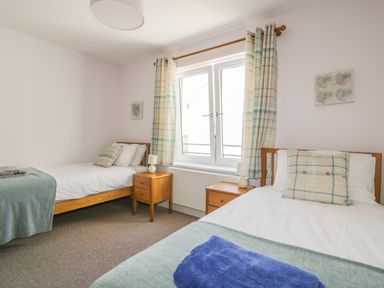 A bedroom with two single beds wooden nightstands and a window with plaid curtains at 5 Ocean Heights in Newquay