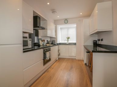A kitchen with white cabinets black countertops a microwave an oven a sink a clock on the wall and flowers on the windowsill at 5 Ocean Heights in Newquay