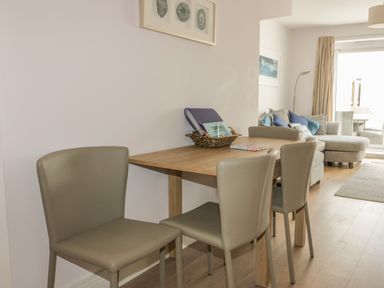 A dining table with four chairs in an open living room with a sofa and cushions at 5 Ocean Heights in Newquay