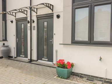 Two dark grey front doors with canopies and a green planter with red flowers outside a building at 5 Ocean Heights in Newquay