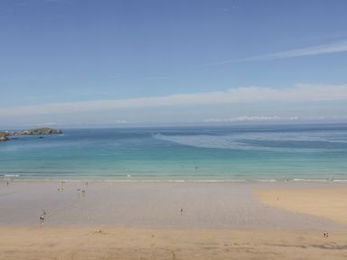 A sandy beach with people near the shore and a view of the sea and a small island at 5 Ocean Heights in Newquay