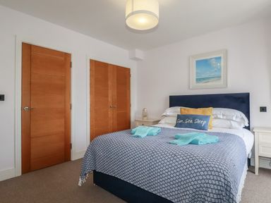 A bedroom with a bed with blue and white bedding two wooden doors and a framed picture on the wall at 5 Ocean Heights in Newquay