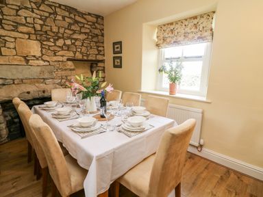 A dining room with a set table and stone wall at Waingate Cottage in Flookburgh
