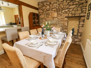 A dining room with a table set for eight people and a stone wall at Waingate Cottage in Flookburgh