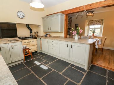 A kitchen with light cabinets a stove a countertop with flowers and a view into a dining area at Waingate Cottage in Flookburgh
