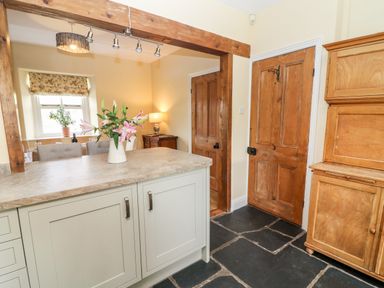 A kitchen area with a countertop vase of flowers wooden doors and a wooden cabinet at Waingate Cottage in Flookburgh