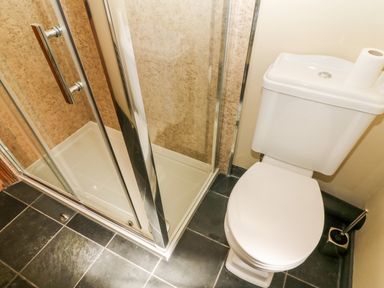 A bathroom with a corner shower enclosure and a toilet with a roll of toilet paper on top at Waingate Cottage in Flookburgh