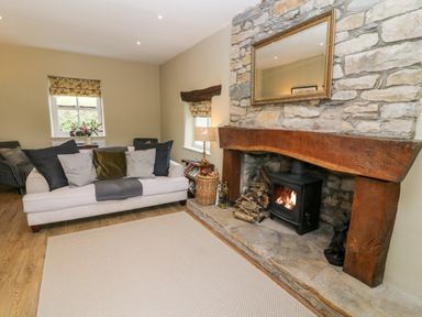 A living room with a fireplace wooden beam mantel white sofa cushions and wooden floor at Waingate Cottage in Flookburgh