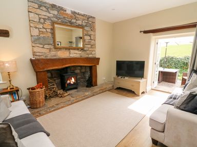 A living room with a stone fireplace a wooden mantel a burning stove a television on a cabinet and sofas at Waingate Cottage in Flookburgh