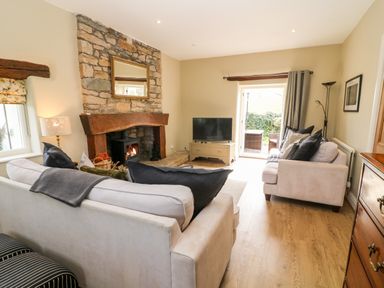 A living room with a stone fireplace two sofas a television and glass doors leading outside at Waingate Cottage in Flookburgh