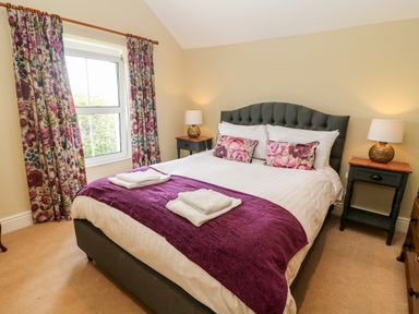A bedroom with a double bed with floral pillows and purple throw with two bedside tables and lamps at Waingate Cottage in Flookburgh
