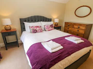 A bedroom with a double bed two bedside tables with lamps a wooden chest of drawers and an oval mirror at Waingate Cottage in Flookburgh