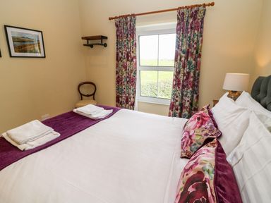 A bedroom with a bed with white linens and floral pillows next to a window with floral curtains at Waingate Cottage in Flookburgh