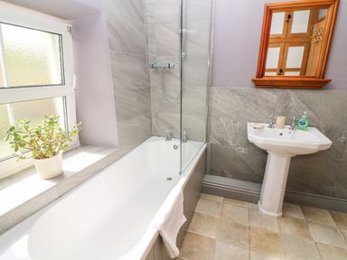 A bathroom with a bathtub shower washbasin mirror and a plant on the window sill at Waingate Cottage in Flookburgh