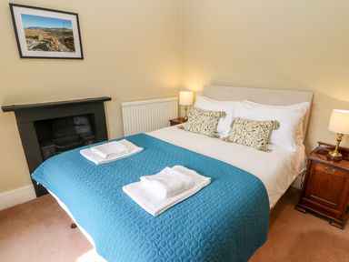 A bedroom with a bed with blue quilt and white towels two lamps and a framed picture on wall at Waingate Cottage in Flookburgh