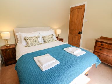 A bedroom with a bed covered with a blue quilt and white towels on top at Waingate Cottage in Flookburgh
