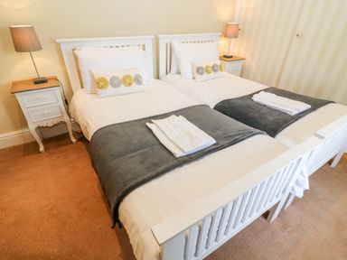 A bedroom with two single beds with white frames nightstands with lamps and folded towels on the beds at Waingate Cottage in Flookburgh
