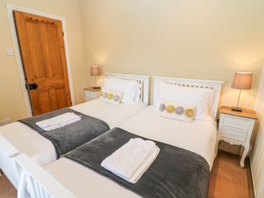 A bedroom with two single beds side by side with white bed frames and bedding at Waingate Cottage in Flookburgh