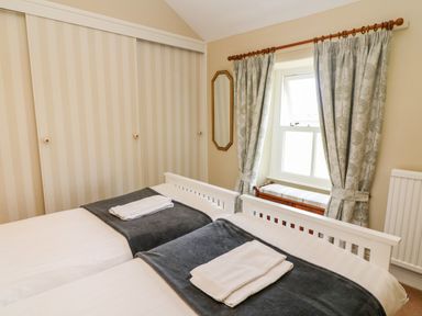 A bedroom with two single beds facing a window with curtains at Waingate Cottage in Flookburgh