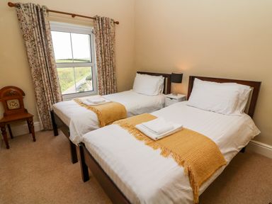 A bedroom with two single beds bedside table with lamp and window with floral curtains at Waingate Cottage in Flookburgh