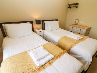 A bedroom with two single beds with white linens and yellow throws at Waingate Cottage in Flookburgh