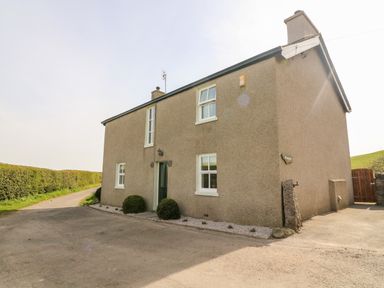 A two story house with a gravel pathway and bushes next to a road at Waingate Cottage in Flookburgh