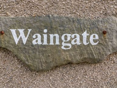 A stone plaque with the word Waingate mounted on a textured wall at Waingate Cottage in Flookburgh