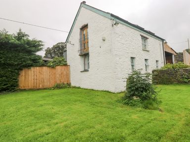 A white stone house with blue trim windows and a green lawn surrounded by wooden fence and trees at Y Cartws in Nevern near Cardigan