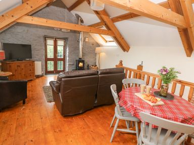 A living room with a brown leather sofa wooden beams a small dining table with a red checkered tablecloth and a wood stove at Y Cartws in Nevern near Cardigan