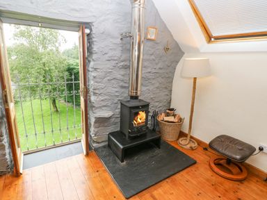 A room with a wood burning stove next to an open door leading outside at Y Cartws in Nevern near Cardigan