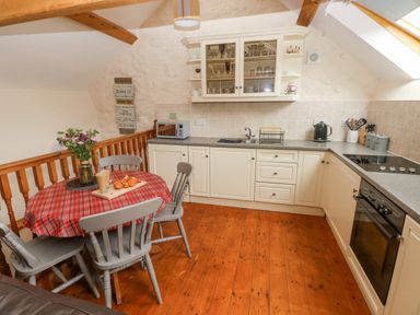 A kitchen with white cabinets a round table with a red checkered tablecloth and gray chairs at Y Cartws in Nevern near Cardigan