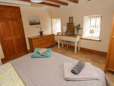 A bedroom with a wooden dresser a white vanity table with a stool two windows and towels on a bed at Y Cartws in Nevern near Cardigan
