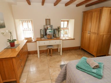 A bedroom with a wooden dresser white vanity table and wooden wardrobe at Y Cartws Nevern near Cardigan