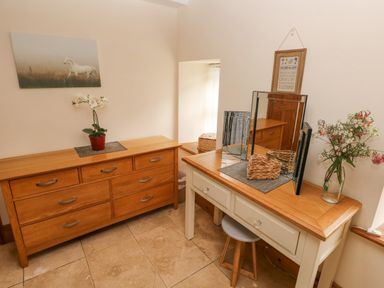A room with wooden dressers a three-panel mirror a stool a plant in a red pot and a vase with flowers at Y Cartws in Nevern near Cardigan