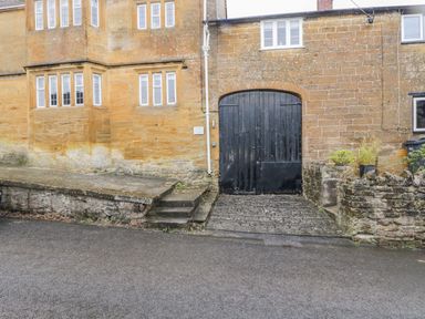 An exterior view of a stone building with multiple windows and a large black wooden gate at Bower Coach House in Bower Hinton near Martock