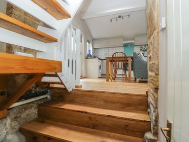 View of wooden stairs leading to a kitchen dining area with a wooden chair a grey sofa and white cabinets at Bower Coach House in Bower Hinton near Martock