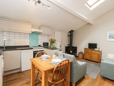 An open kitchen and living area with a wooden dining table set for two a wood burning stove and a small TV on a wooden cabinet at Bower Coach House in Bower Hinton near Martock