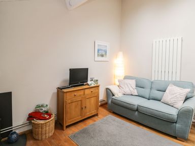 A living room with a light blue sofa two pillows wooden cabinet with television standing lamp and a basket at Bower Coach House in Bower Hinton near Martock