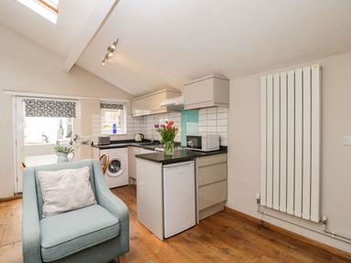 A small kitchen area with a refrigerator washing machine microwave and a chair at Bower Coach House in Bower Hinton near Martock