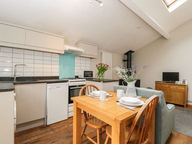 A kitchen and dining area with a wooden table set for two and a sofa at Bower Coach House in Bower Hinton near Martock