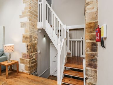 A wooden staircase with white railings between stone pillars and a table with a lamp in a hallway at Bower Coach House in Bower Hinton near Martock
